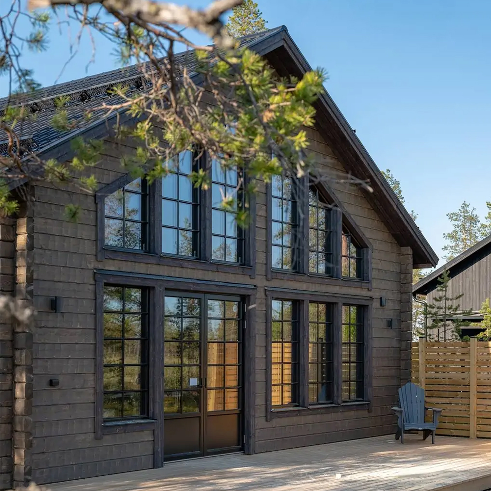 Exteriör av arkitektritad fjällstuga med timmerpanel och stora fönster.